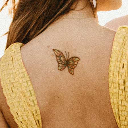 Colorful butterfly tattoo on back of girl who is wearing a yellow dress