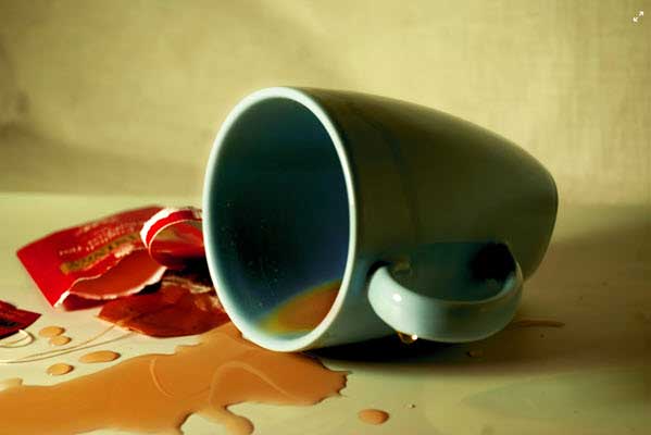 coffee spill | Gardens with Wings A tipped dark mug with coffee spilled across a light table, red wrappers and coins scattered nearby.