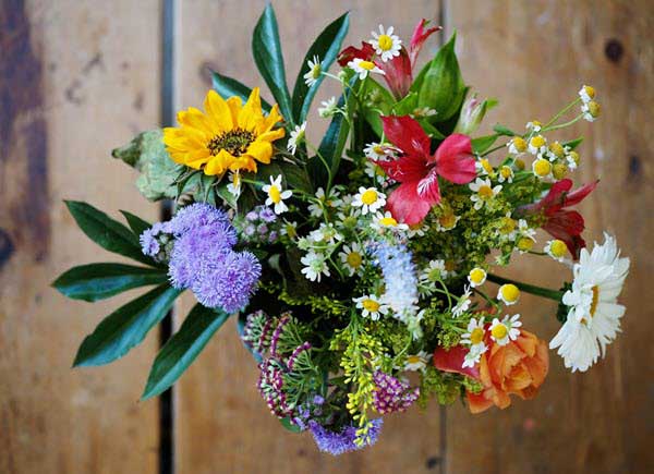 colorful flower bouquet | Gardens with Wings Colorful mixed bouquet with sunflowers, daisies, red lilies, purple and orange flowers against a wooden background.