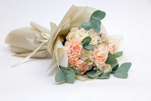 flower bouquet | Gardens with Wings Bouquet of peach and white roses with eucalyptus, wrapped in cream paper on a white background.