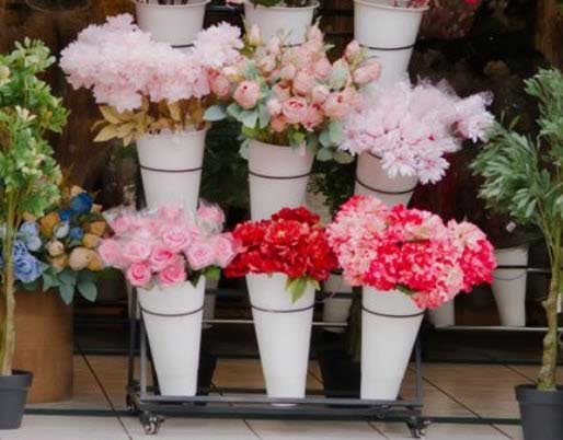 Display of colorful flowers arranged in white cone vases on a metal stand, pink and red blooms with greenery on a shop floor.