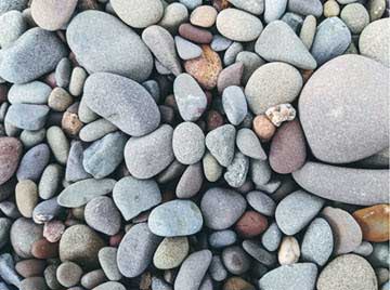 Close-up of smooth, colorful pebbles in gray, blue, and earth tones on a beach surface.