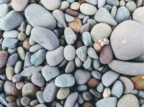 gravel | Gardens with Wings Smooth, rounded pebbles in gray, blue, and brown cover a beach surface in varying sizes and textures.