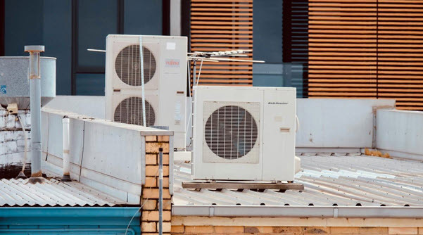 hvac roof | Gardens with Wings Two white outdoor HVAC units on a rooftop with a metal deck and brick parapet against a building facade.