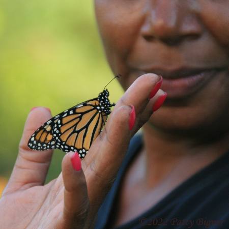 Black lady grins as she holds a Monarch in her hand