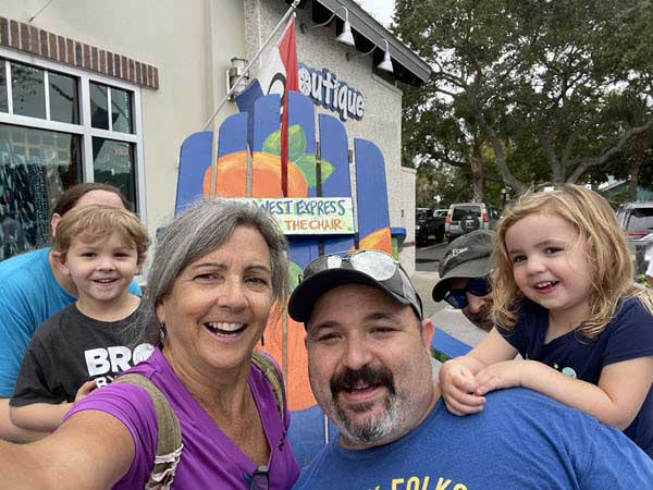 multi generations | Gardens with Wings Smiling family posing for a selfie outside a boutique with a bright mural behind them.
