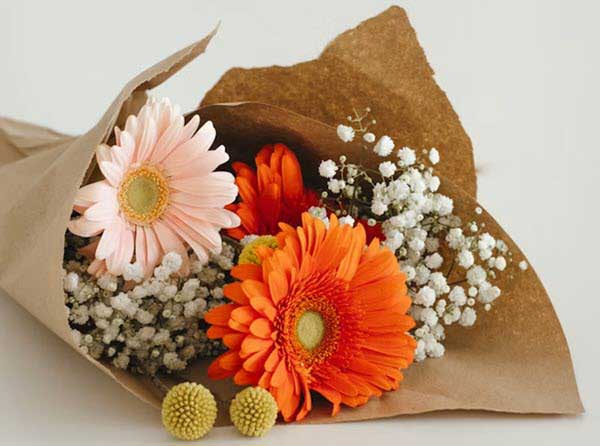 small flower bouquet | Gardens with Wings Bouquet of orange and pink gerbera daisies with white baby's breath, wrapped in brown kraft paper.