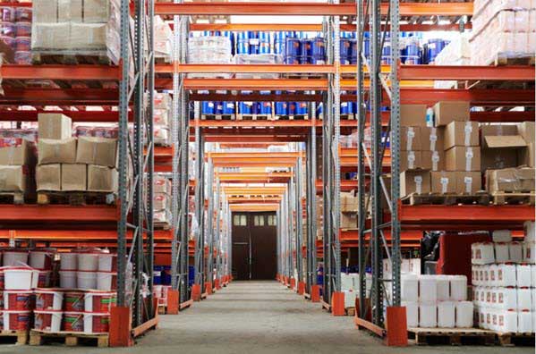 storage equipment | Gardens with Wings A wide warehouse aisle with tall orange metal shelving loaded with boxes and crates on both sides.