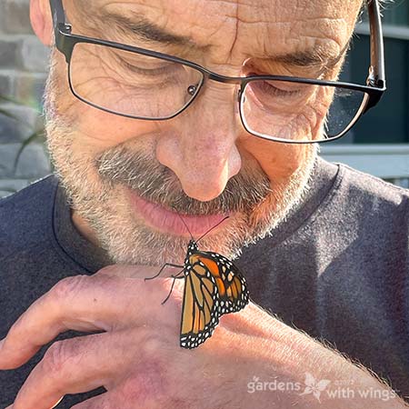 Monarch butterfly perched on a hand of an older man while appearing to be talking to him