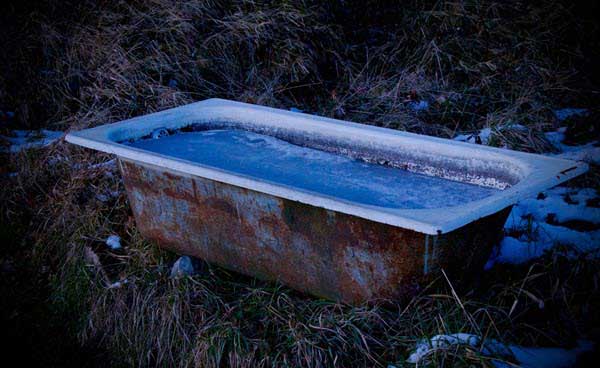 tub | Gardens with Wings Rusty, old bathtub filled with blue water outdoors, surrounded by grass and a hint of snow in a natural setting.